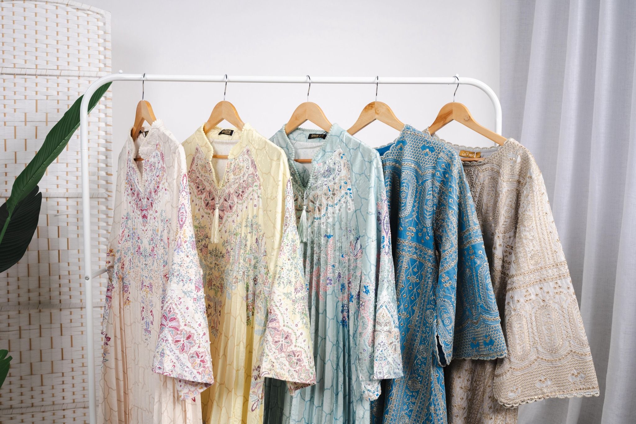 Lima jalabiya bersulam tergantung di rak putih studio Habibti: krim, kuning, mint, biru dan beige