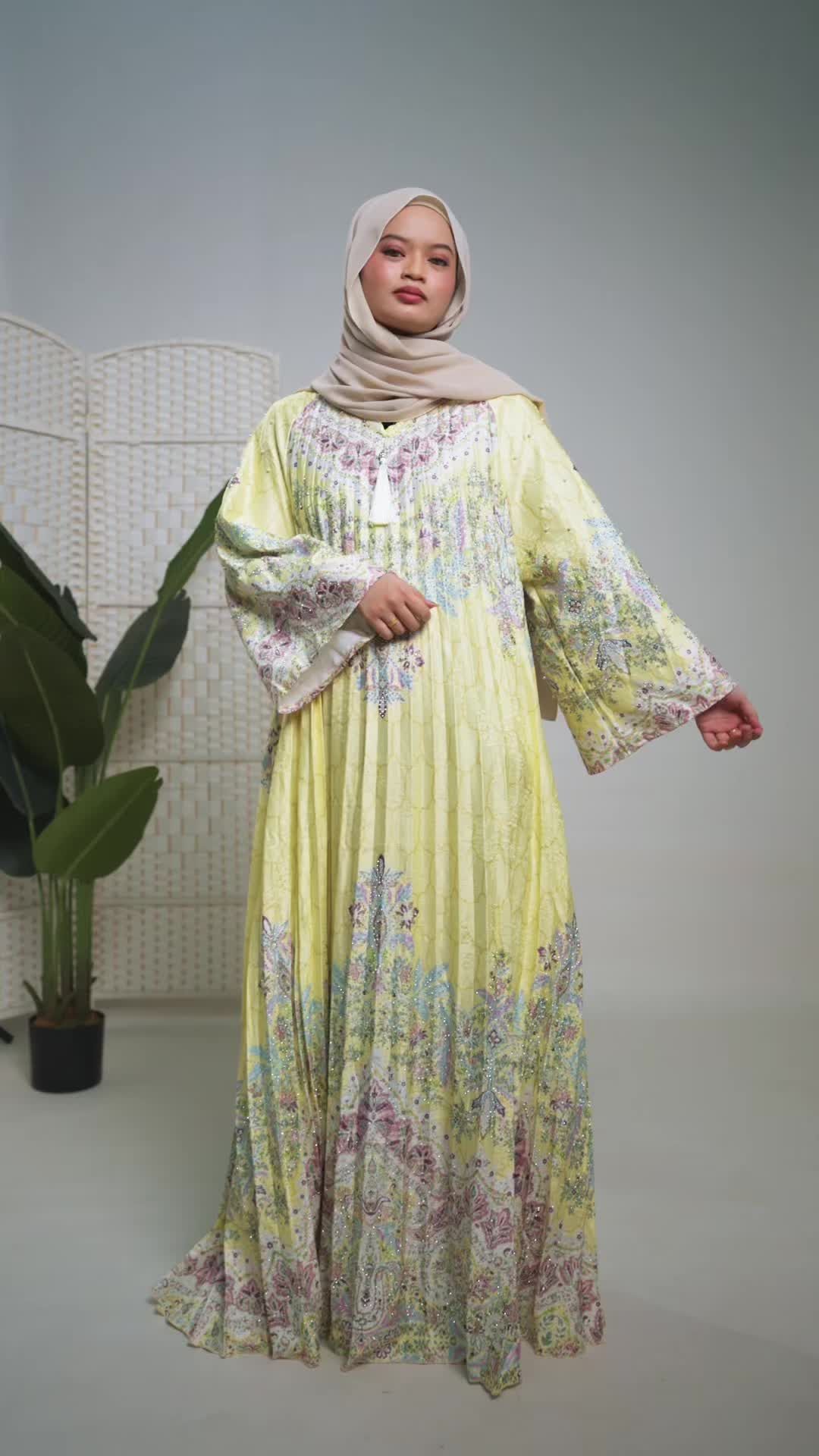 Jalabiya pleated kuning bercorak pink dan biru dengan tassel di leher, dipakai model