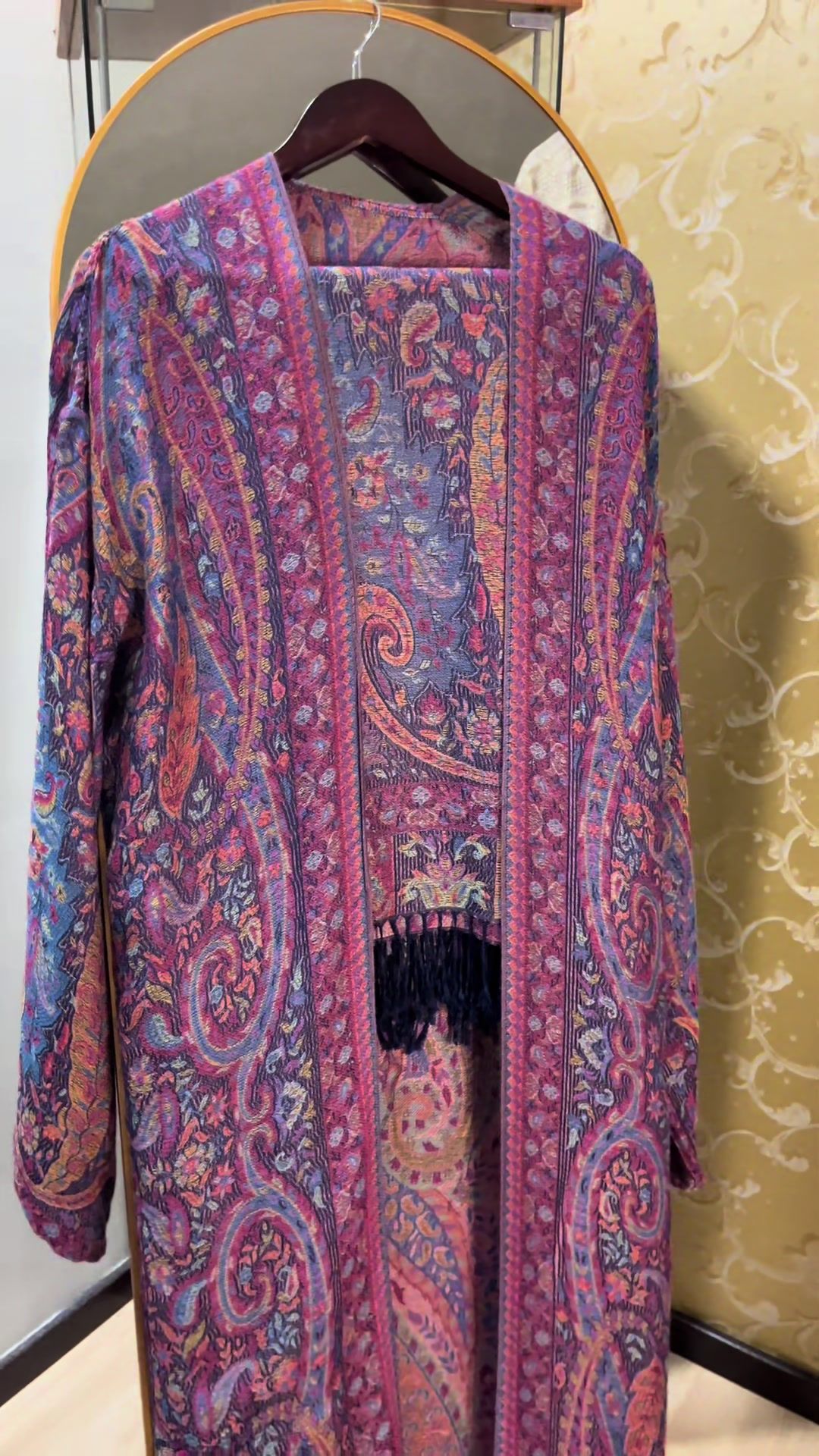 Jalabiya pashmina ungu magenta bercorak paisley dengan jumbai, tergantung pada penyangkut kayu
